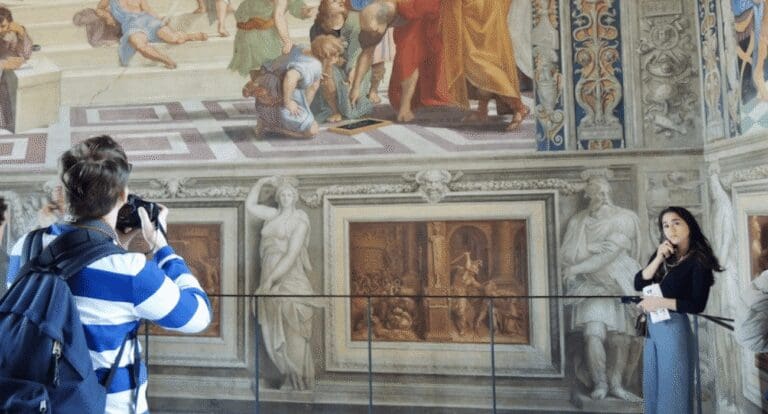 A man takes a photo while a woman listens to an audio guide inside the Raphael rooms