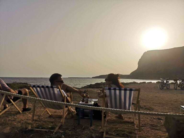 A couple sit on athe beach enjoying sunset at Ferragosto