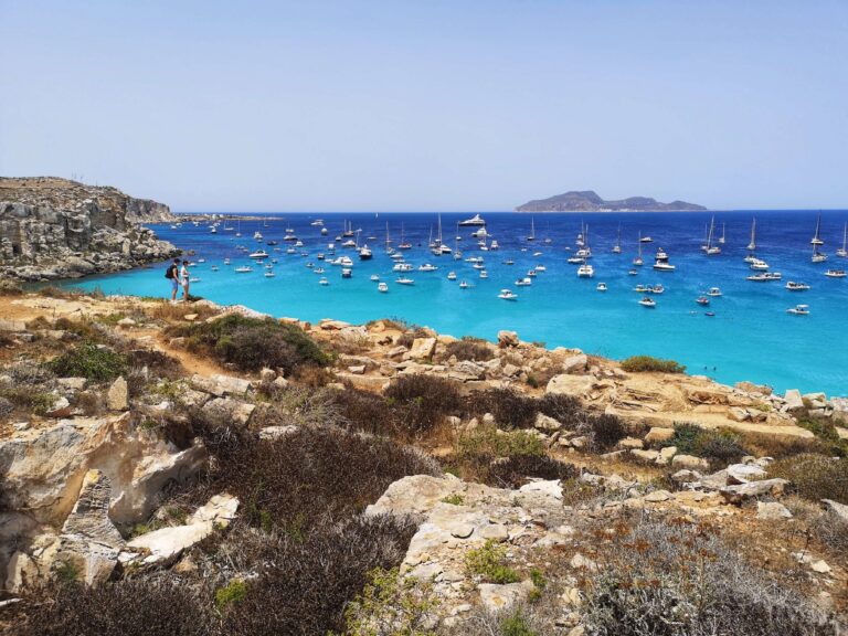 boats bob in the azure water as a couple enjoy a hike during ferragosto