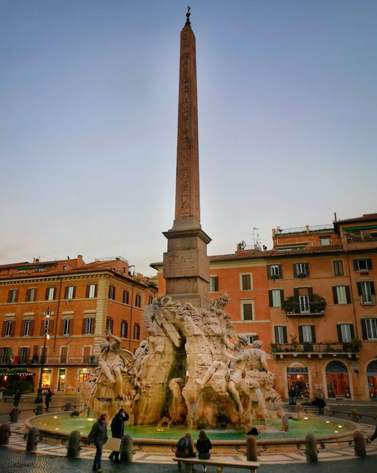 view of the fountain of the four rivers in piazza navona in rome with ochre colored buildings in the background
