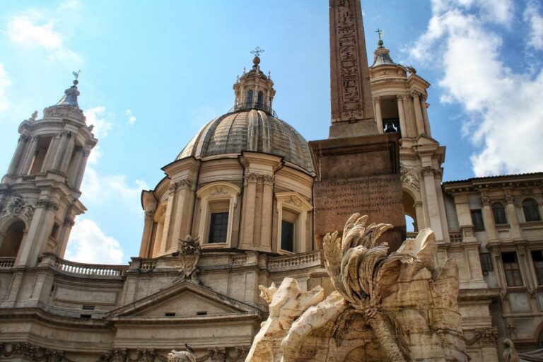 Photo of the base of the obelisk of the fountain of the four rivers in piazza navona in rome with the dome of the church of st. agnes in agone in the background