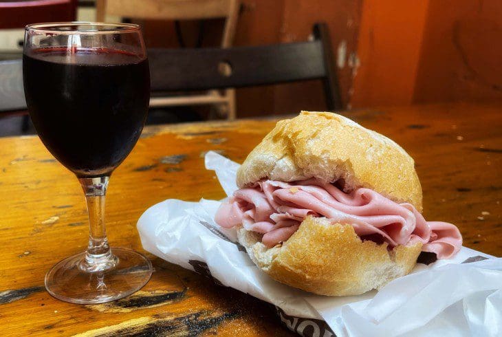 Mortadella Panino woth a glass of red wine on a wooden counter in a Roman sandwich shop