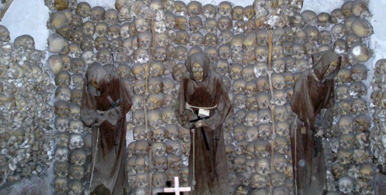 The Capuchin Crypt in Rome showing the skeletons of three robed friars in niches made from human skulls