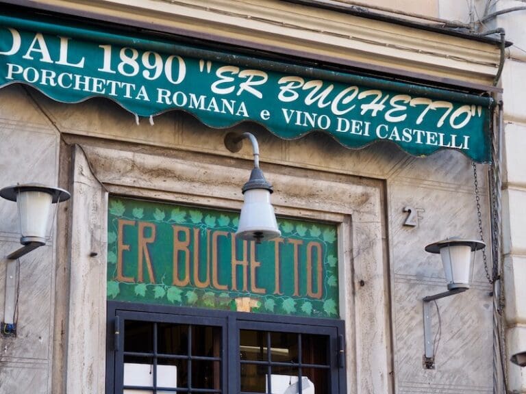 View of the facade of Er Buchetto in Rome showing the green shop sign and awning with the date 1890, the year the shop opened
