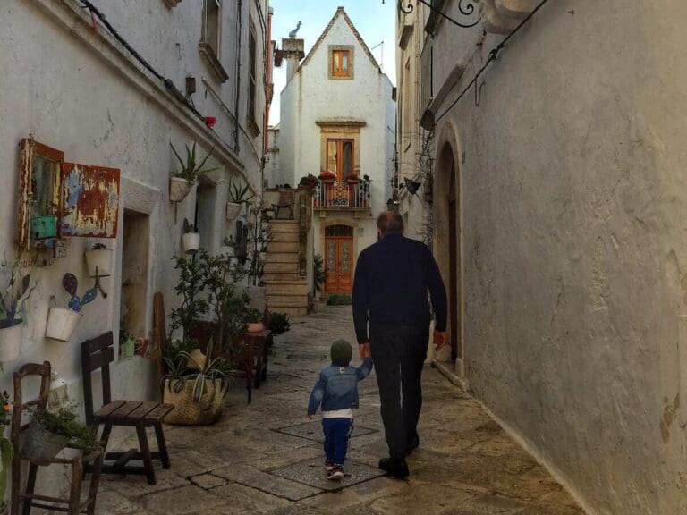 a father and son walk down an alley in locorotondo