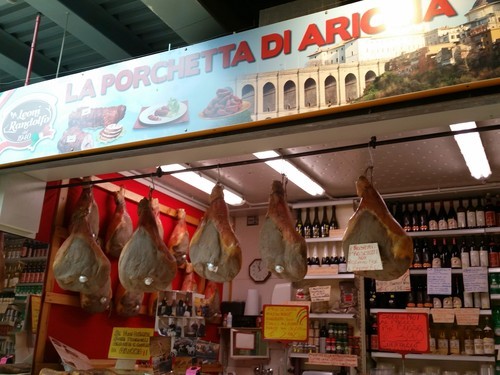 Porchetta stand in Tronfale market Rome with prosciutto hanging from the ceiling