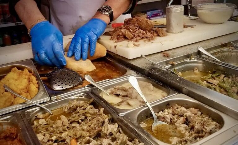 Food counter at Mordi e Vai showing the vendor preparing a panino with vats of fillings in front of them