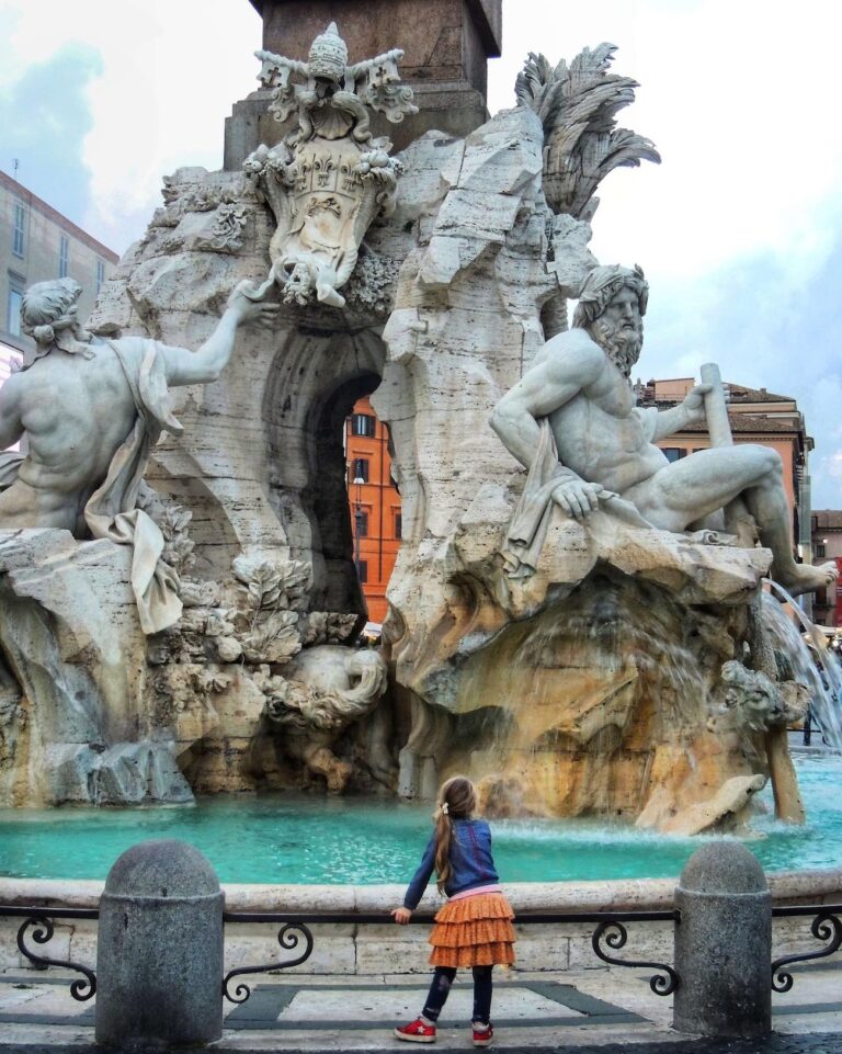 small child standing in front of the fountain of the four rivers in piazza navona in rome