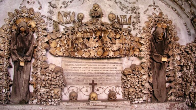 Crypt of the Capuchins Rome showing two robed skeletons of friars and an artistic display of bones including three smaller skeletons holding winged hourglasses