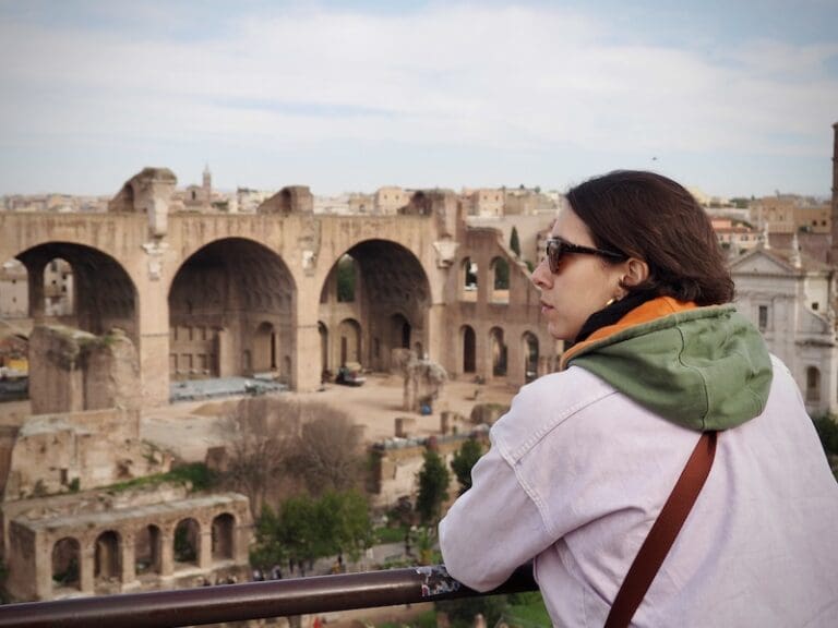 a visitor looks out over the roman forum with the basilica of maxentius in the background