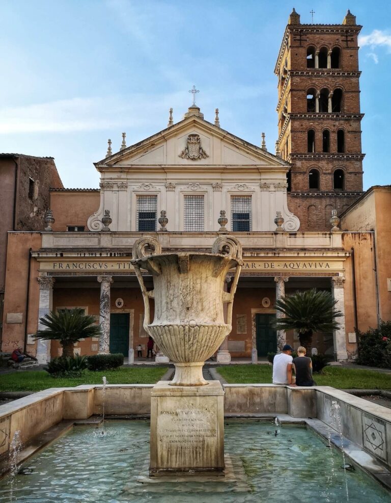 Courtyard of the church of Santa Cecilia in Trastevere Rome showing a fountain with a Roman era marble vase in the foreground and the brick medieval bell tower of the church in the background