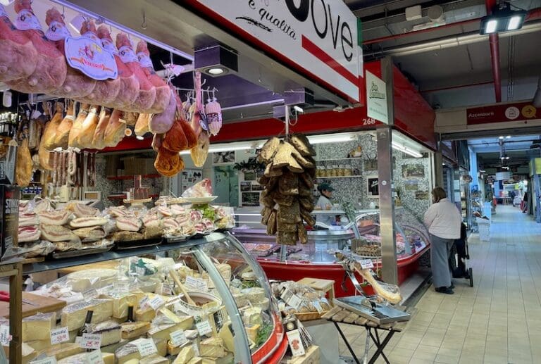 Trionfale market in rome showing hanging proscuitto and guanciale and a selection of cheeses at one of the stalls