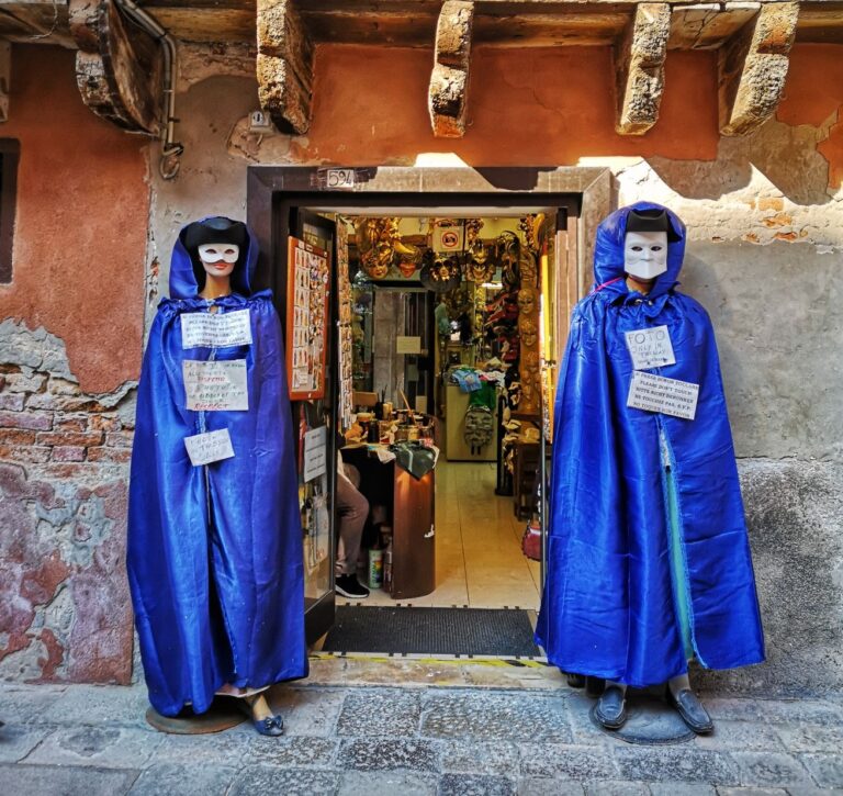 Shop front in Venice showing two mannequins dressed in purple robes wearing the Bauta style Venetian Carnival mask