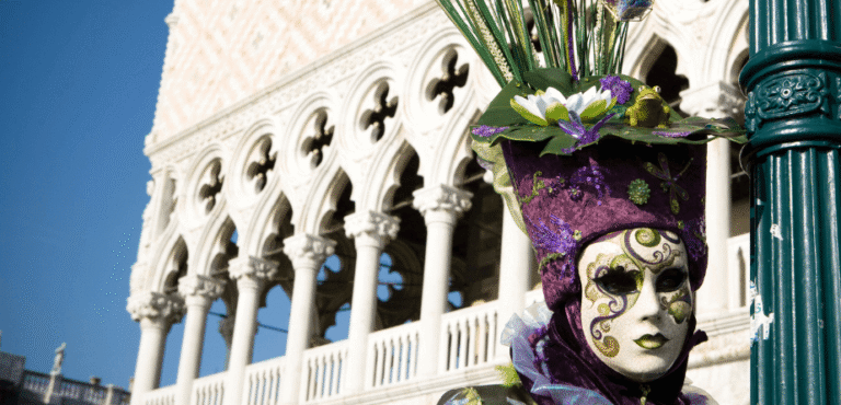 Venetian Canival goer wearing as mask and purple hat with green foliage head-dress and a Venetian Palazzo in the background