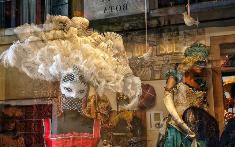 Window front of a store in Venice showing the Colombina style Venetian Carnival mask in white with an elaborate feather plume