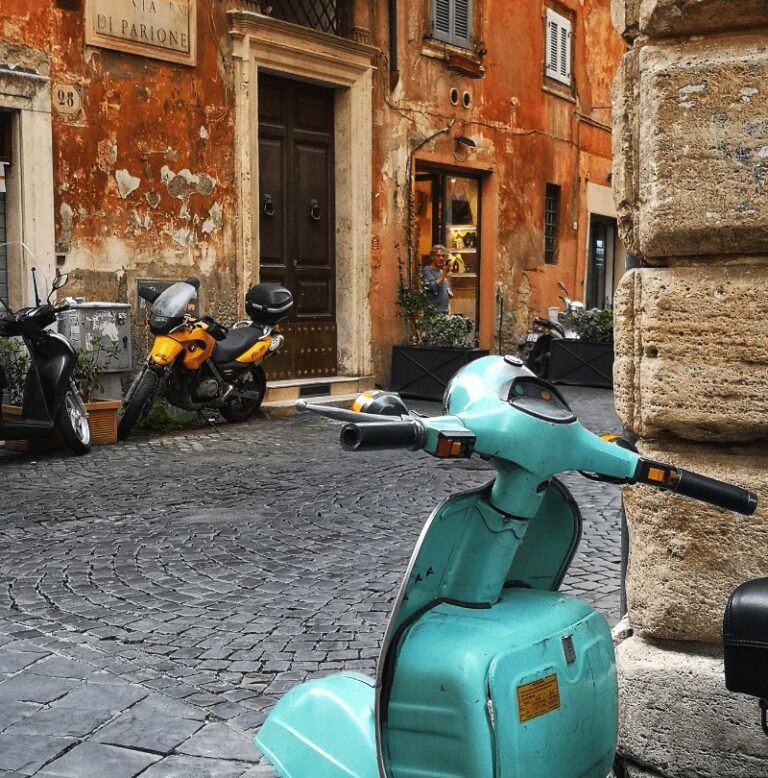 Via Governo Vecchio Rome with a turquoise coloured vespa in the foreground and ochre coloured Renaissance building in the background and cobbled alleys