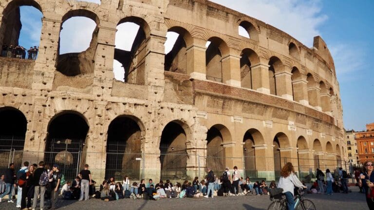 students and visitors sit outside the colosseum in rome