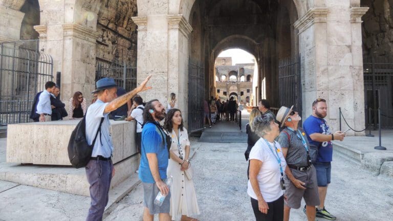 a colosseum group listens to a guide's explanation beneath the arches of the amphitheater
